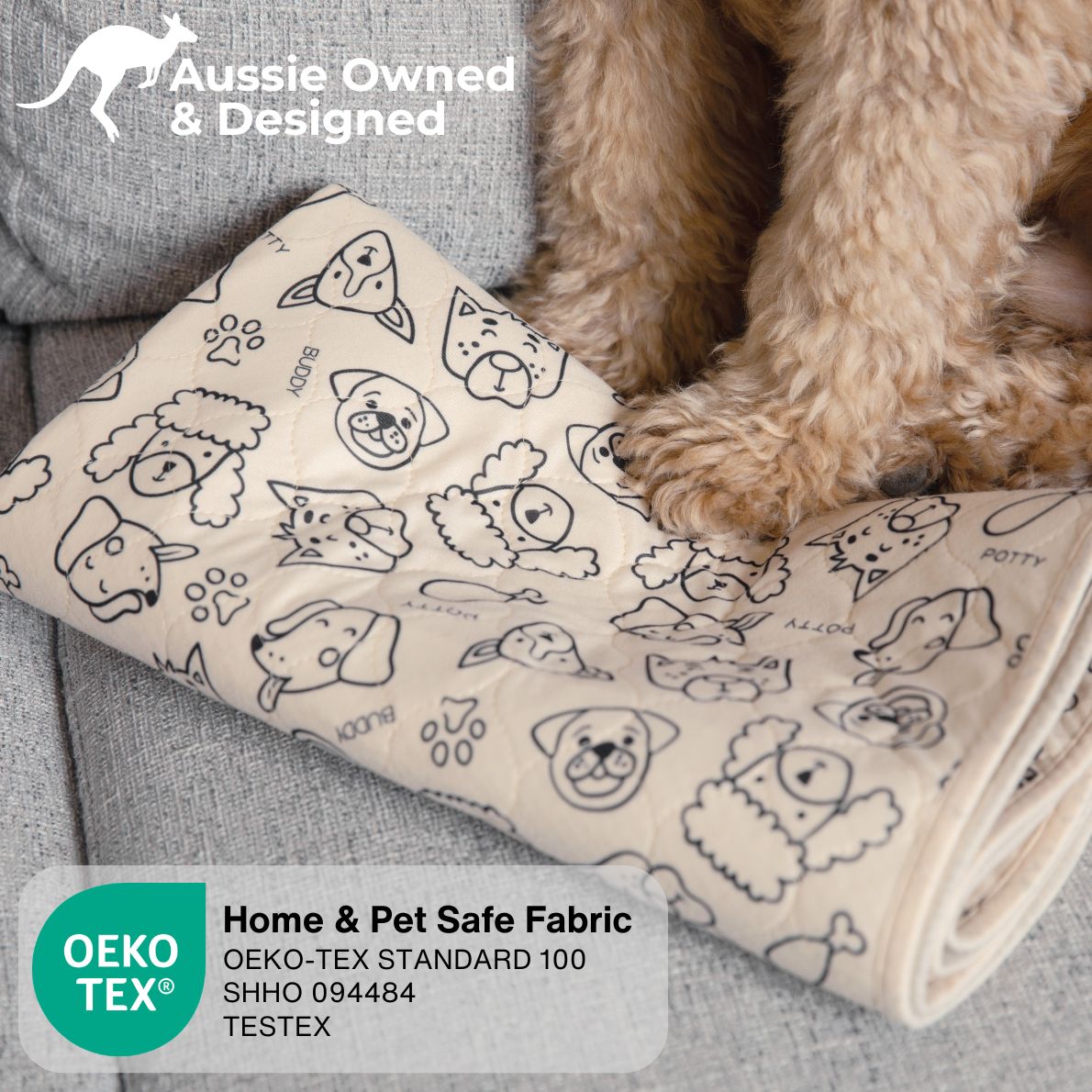 A beige pet blanket with black line drawings of dog faces, potty training symbols, and paw prints, shown on a gray sofa with a fluffy light brown dog's legs visible. Text overlays include 'Aussie Owned & Designed', 'Home & Pet Safe Fabric', and OEKO-TEX certification details.
