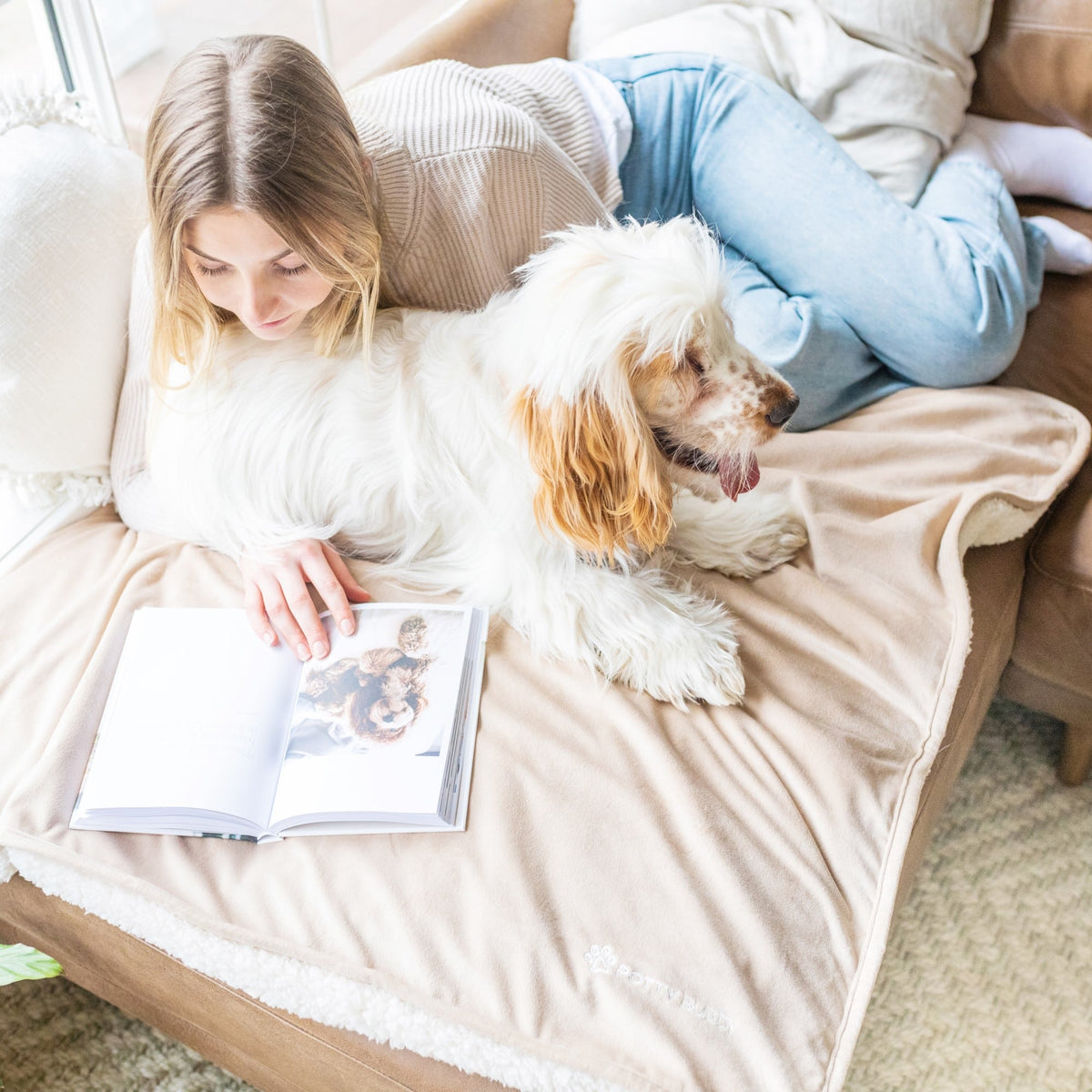 A dog and its owner relaxing on the couch with a Potty Buddy Waterproof Blanket underneath them